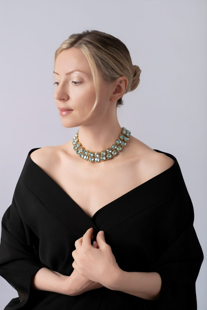 Woman wearing blue crystals necklaces with off the shoulder black kimono on a light blue background.