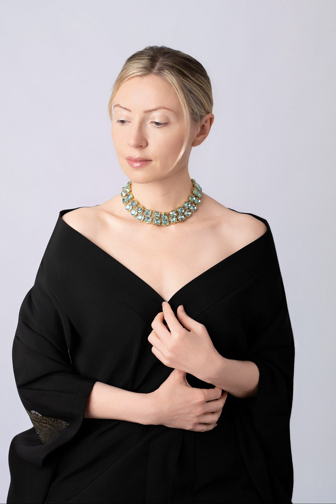 Woman wearing blue crystals necklaces with off the shoulder black kimono on a light blue background.