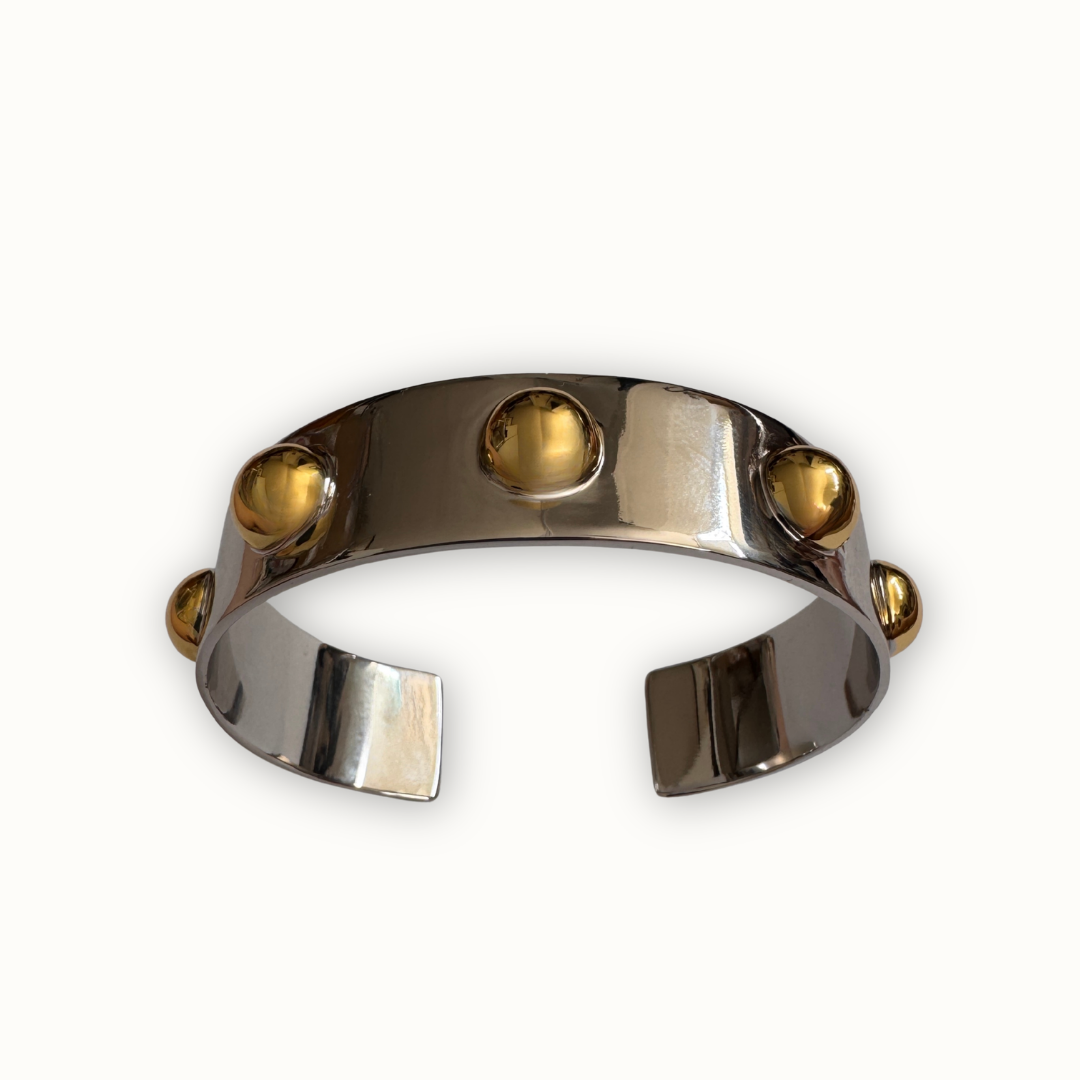 Silver Roman cuff bracelet with polished gold-tone dome accents on ivory background
