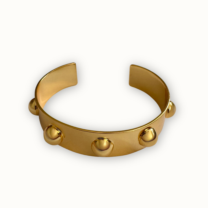 Gold sculptural Roman open cuff bracelet with polished dome accents on a clean ivory background
