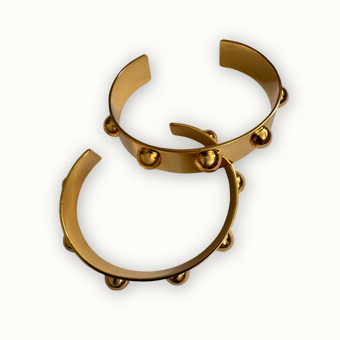 Two gold sculptural Roman open cuff bracelets with polished dome accents on a clean neutral background