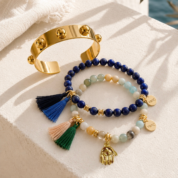 Gold sculptural Roman cuff bracelet styled with lapis lazuli and natural stone beaded bracelets with tassels in warm sunlight