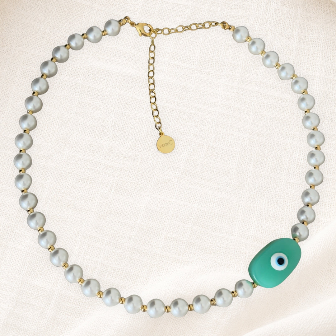 18K Gold plated pearl necklace with handcrafted aqua toned evil eye bead on white linen background.