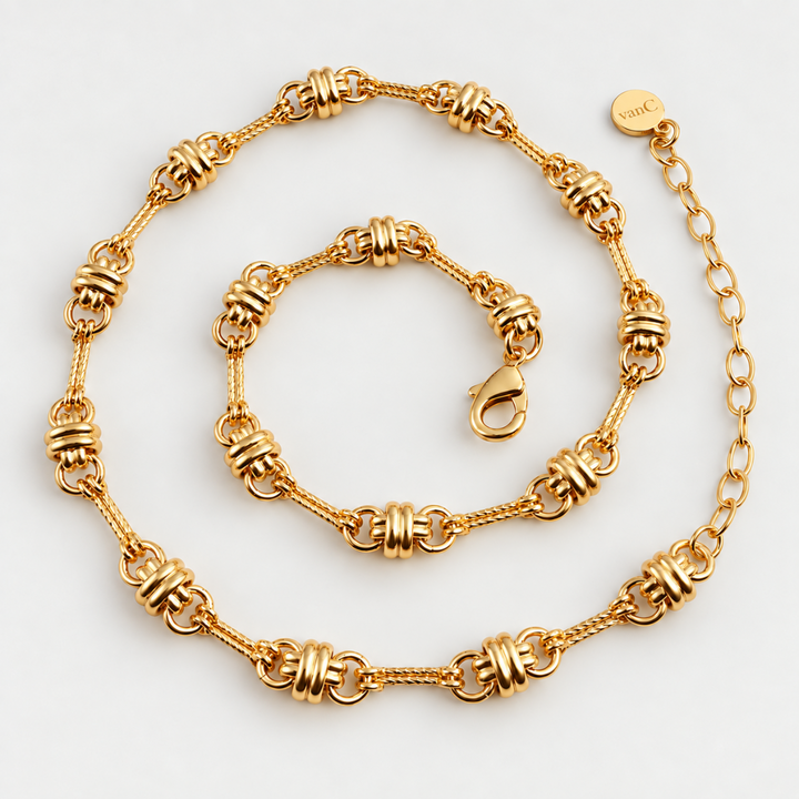 Gold plated chunky bohemian chain featuring textured cylindrical links and a coiled chain extender, displayed on a clean white background. A round tag on the clasp is engraved with the brand logo “vanC”.