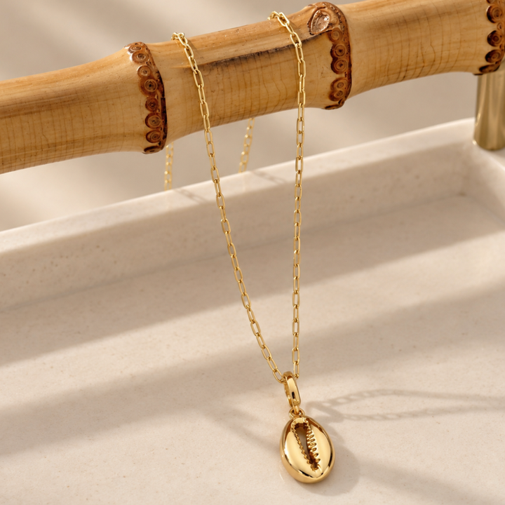 Gold plated jewellery look from Blauw van C jewellery brand, including the Classic link chain with the Fortune Teller charm pendant, draped over a bamboo holder tray with light beige stone surface. 