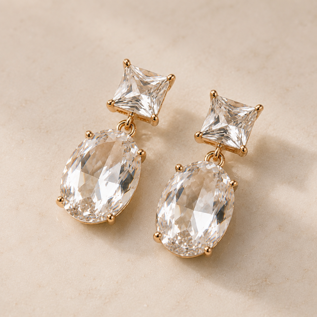  Faceted clear gold plated crystal earrings resting on neutral stone with square-cut studs and large oval crystal drops.