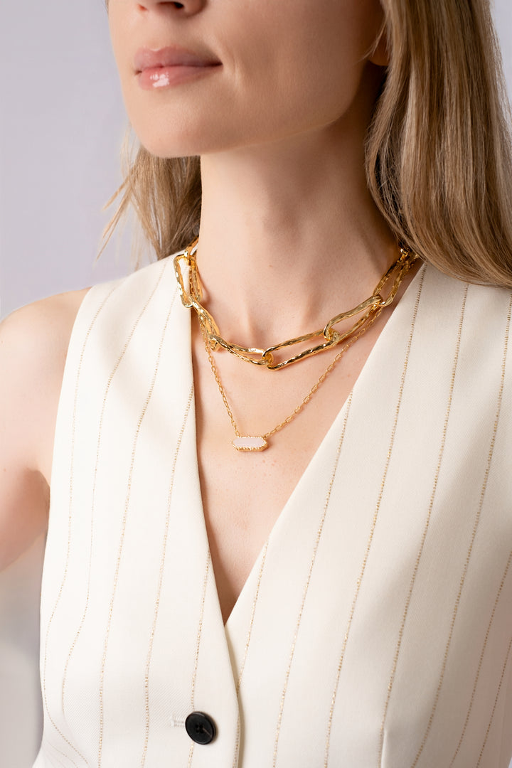 Gold Connecting Worlds Necklace with pearl drop layered with Andalus necklace with pink stone pendant, worn by a woman with a cream vest