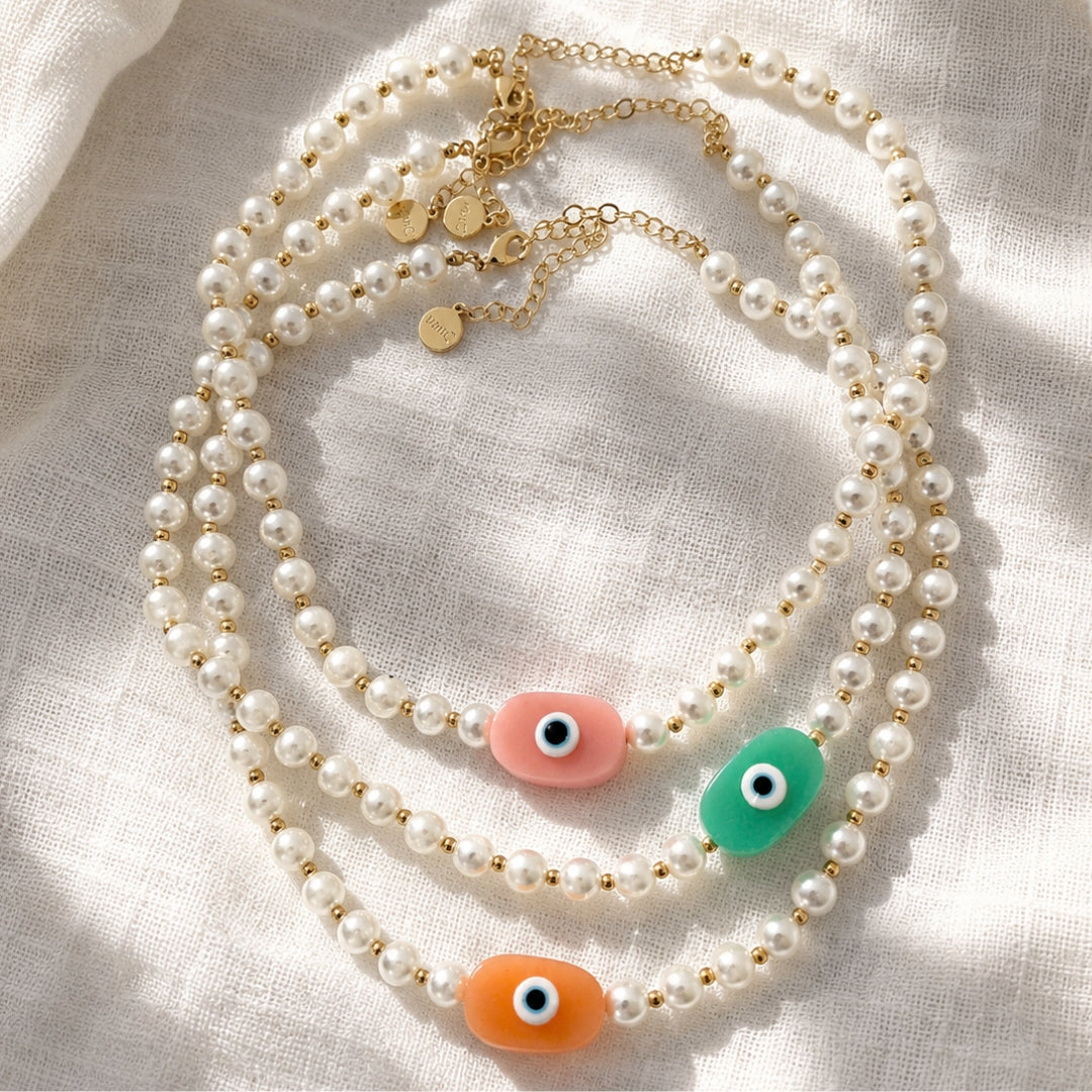 18K Gold plated pearl necklaces with soft pink ,acqua and peach oversized evil eye pendants on white linen shaded background.