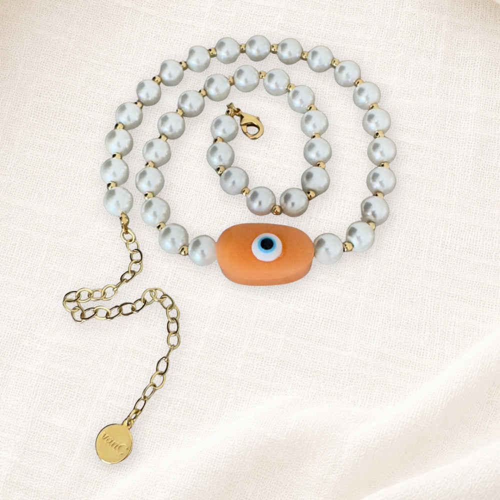 18K Gold plated pearl necklace with peach evil eye oversized handcrafted bead on white linen background.