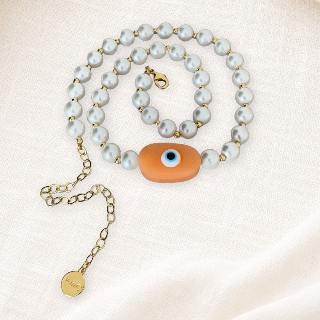 18K Gold plated pearl necklace with peach evil eye oversized handcrafted bead on white linen background.
