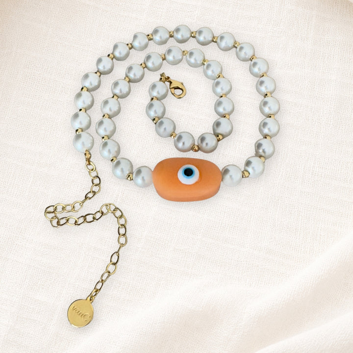 18K Gold plated pearl necklace with peach evil eye oversized handcrafted bead on white linen background.