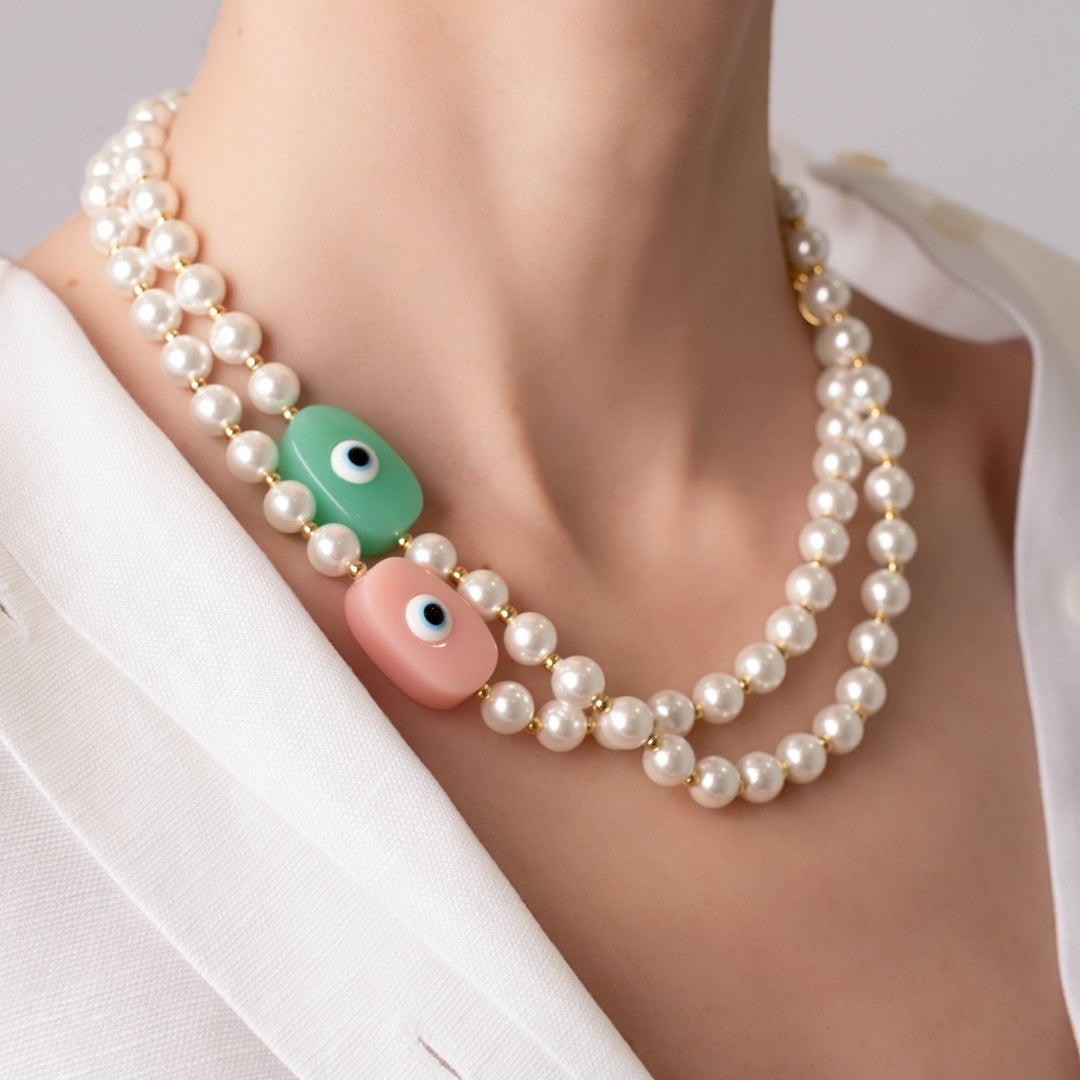 18K Gold plated pearl necklaces with pink and aqua pastel toned evil eye pendants worn with white linen shirt.
