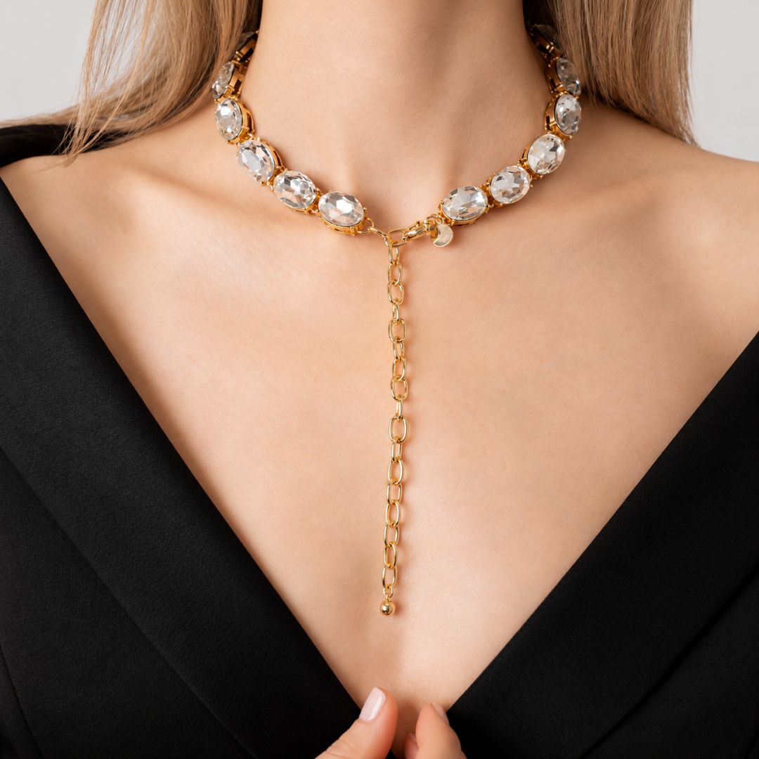 Close-up of the Glow Oversize Crystal Necklace with white crystals and 18-karat gold plating, worn with the clasp at the front and extension chain hanging over a black V-neck outfit.