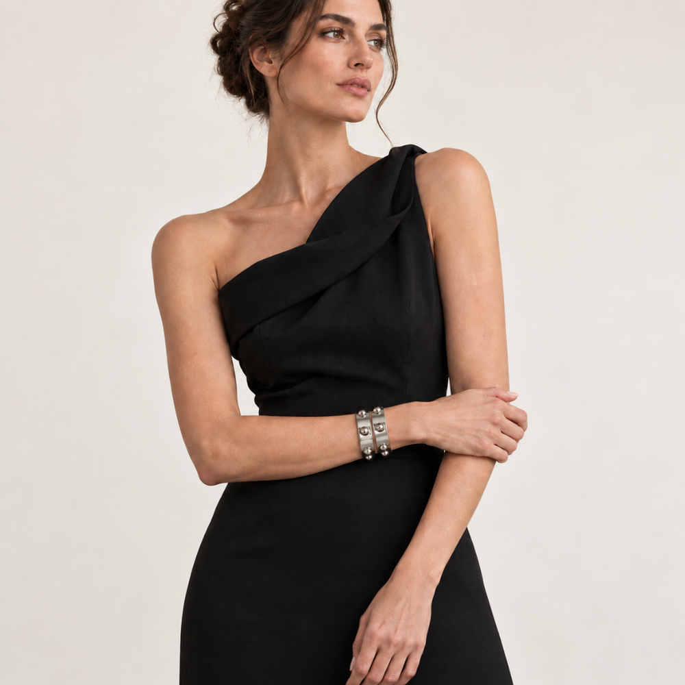 Model wearing a black sleeveless elegant dress and two Roman Cuff bracelets in silver, on a pale background 
