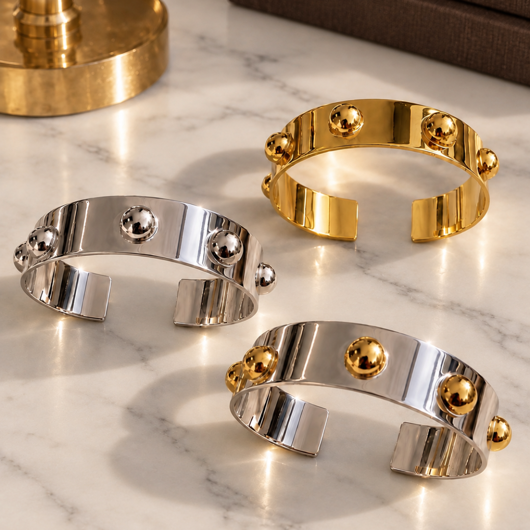Three Roman Cuff bracelets in three different finishes Gold 18K Gold plated, Silver Rhodium plated and Silver with Gold displayed on Carrara marble near a brass lamp