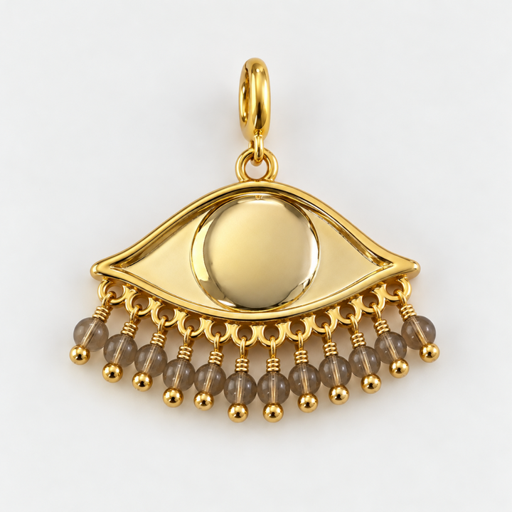 Gold plated See the world eye-shaped pendant with dangling sand toned beads, photographed on a clean neutral background.
