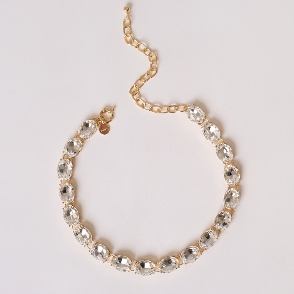 Gold plated necklace with white crystal on a light gray background.