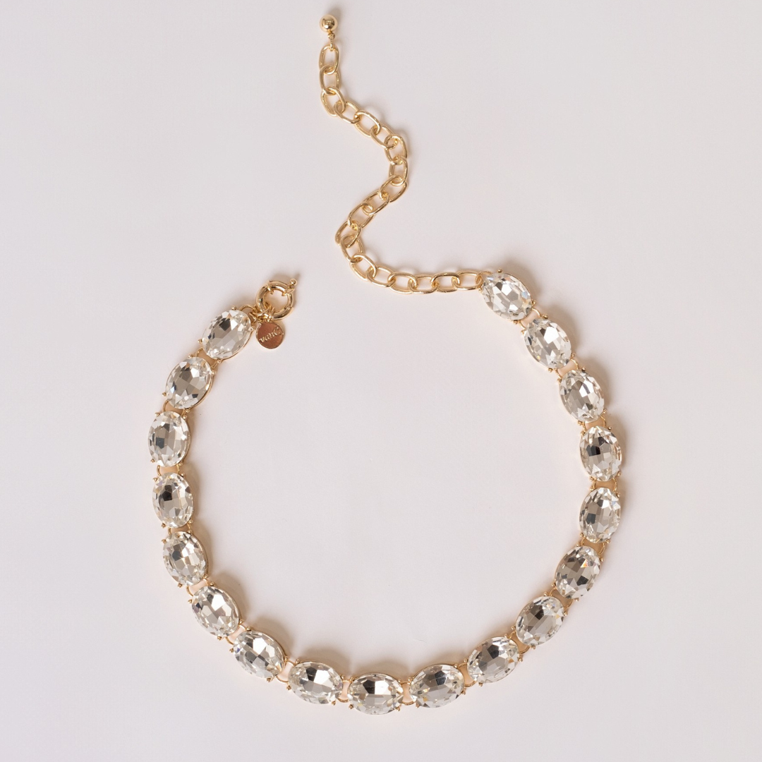 Gold plated necklace with white crystal on a light gray background.
