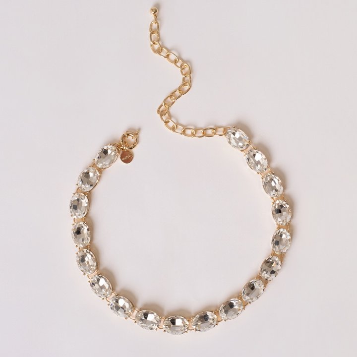 Gold plated necklace with white crystal on a light gray background.