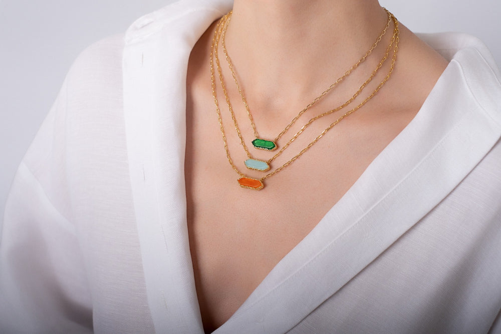 Gold Andalus necklaces with green, blue and orange stones layered on a woman wearing white shirt