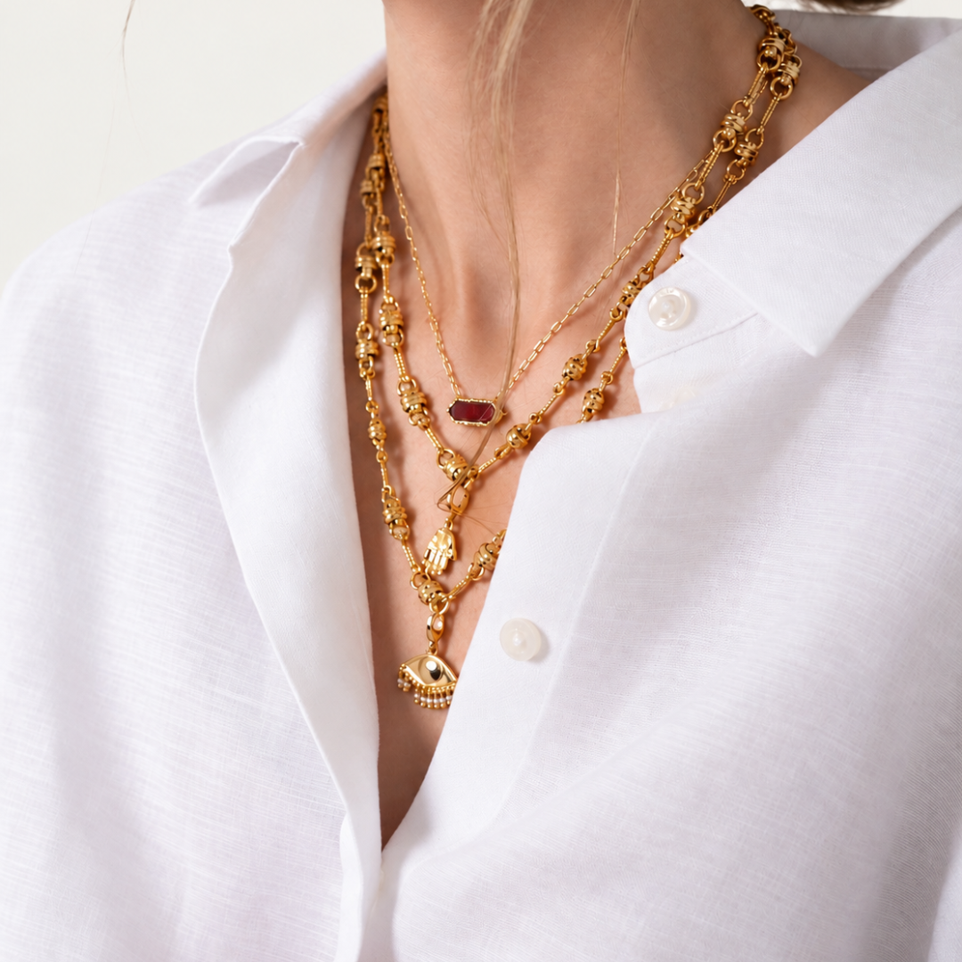 Blauw van C Andalus Gold plated Necklace with Pomegranate Red natural stone pendant, layered with gold charm necklaces on a model wearing a white shirt.