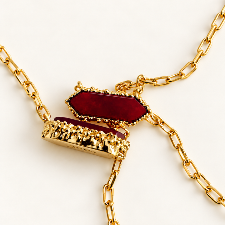 Close-up of two Blauw van C Andalus pendants in Pomegranate Red, showing the faceted agate, textured gold-plated settings and link chains.