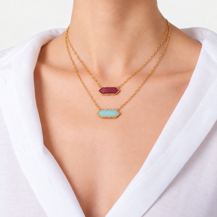 Blauw van C Andalus necklaces in Pomegranate Red and Cadiz Blue, layered on gold-plated link chains with a white shirt.